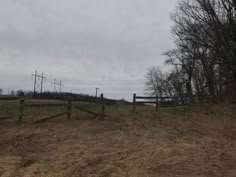 an empty field with a fence and trees in the background on a gloomy day