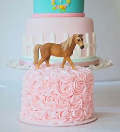 a pink cake with a horse figurine on top is sitting on a table