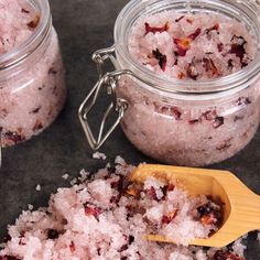 two jars filled with pink salts next to a wooden spoon on a black counter top