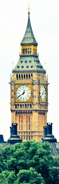 the big ben clock tower towering over the city of london on a cloudy day with trees in foreground