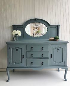 a blue dresser with a mirror on top of it next to a vase and flowers