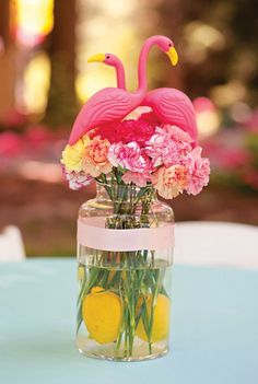 a vase filled with flowers and pink flamingos sitting on top of a blue table