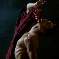 a man with no shirt holding grapes in his hand and wearing a red robe around his neck