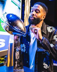 a man holding a football trophy in his right hand and looking at the ball he is holding