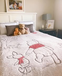 two teddy bears sitting on top of a bed with a white comforter and pillows