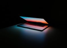 an open laptop computer sitting on top of a table in the dark with light coming from it's screen