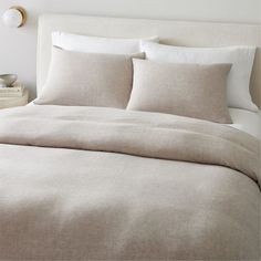 a bed with white linens and pillows in a neutral colored bedroom, next to a night stand