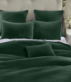 a bed with green comforters and pillows in a white room next to a night stand