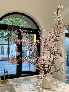 a vase filled with pink flowers sitting on top of a counter next to a window