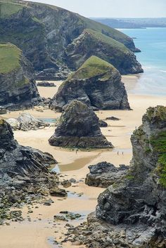 a sandy beach next to the ocean with large rocks