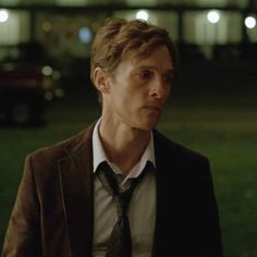 a man wearing a suit and tie standing in front of a green field at night