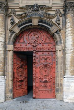 an ornate red door is open on a stone building