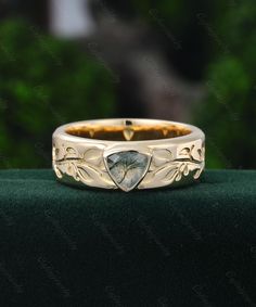 a wedding band with an intricate design and a pear shaped stone in the center, on a green velvet surface