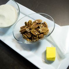 two bowls filled with nuts and butter on a plate next to a block of butter