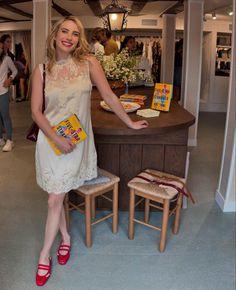 a woman standing in front of a counter with books on it and two stools