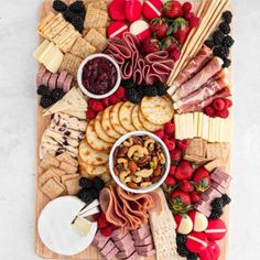 an assortment of cheeses, crackers and fruit on a wooden platter