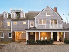 a large gray house with lots of windows and white trim on the front door is lit up at night