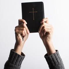 two hands holding up a black book with a cross on it