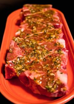 a piece of meat with seasoning on it sitting on an orange plate in front of a black background