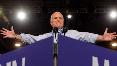 a man standing at a podium with his arms wide open in front of microphones