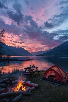 there is a campfire and picnic tables near the water at sunset with mountains in the background