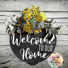 a welcome sign with yellow and black bows on it next to a wooden background that says, welcome to our home