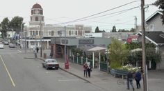 people are walking on the sidewalk in front of shops and buildings with a clock tower