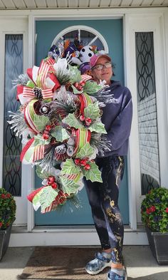 a woman standing in front of a blue door holding a christmas wreath with decorations on it