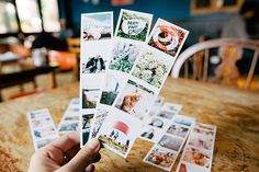 a person holding up several different pictures on top of a wooden table in front of them