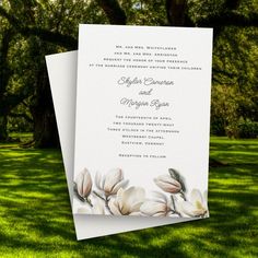 a wedding card with white flowers on the front and back, sitting in green grass