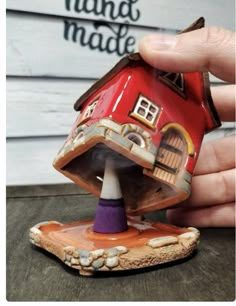 a hand holding a small red house on top of a wooden table