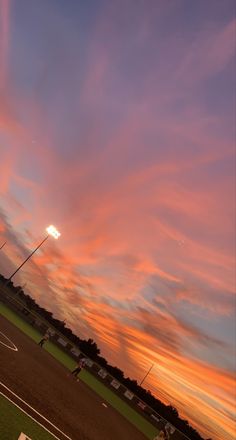 a baseball field at sunset with the sun setting in the distance and some players on the field