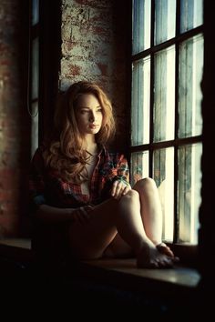 a beautiful young woman sitting on top of a window sill next to a brick wall