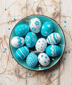 a bowl filled with blue and white decorated eggs on top of a wooden table next to sprinkles