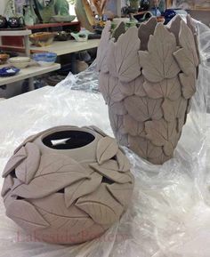 two clay vases sitting on top of a table covered in plastic wrap and paper