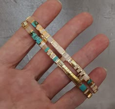 a person is holding three different bracelets in their hand, one with turquoise and the other gold