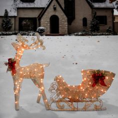 two lighted reindeer sleighs in front of a house on a snowy day