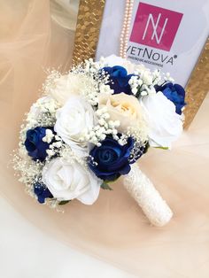 a bridal bouquet with blue and white flowers in front of a gold framed photo