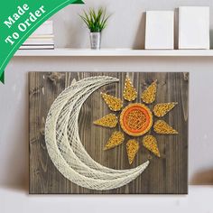 a string art sun and moon on a wooden shelf next to a potted plant