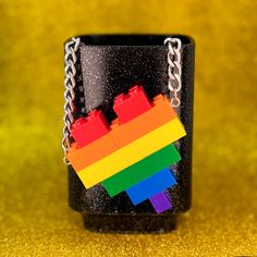 a lego mug with a rainbow colored block on the front and chain attached to it