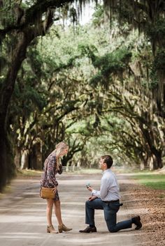 a man kneeling down next to a woman on a road with trees in the background