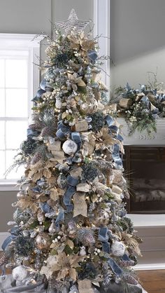 a decorated christmas tree with blue and silver ornaments on it in a living room next to a fireplace