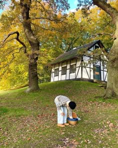 two people standing in front of a tree with leaves on the ground and one person bending over