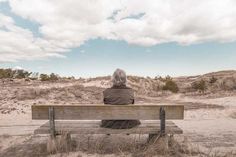 an old man sitting on a bench in the sand dunes looking out at the beach