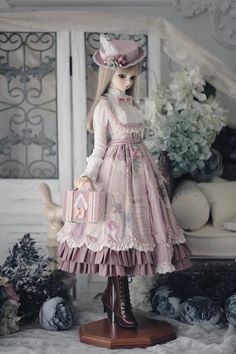 a doll is dressed in pink and holding a suitcase