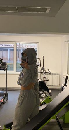 a person wearing a hoodie taking a selfie in a gym with treadmills and exercise equipment