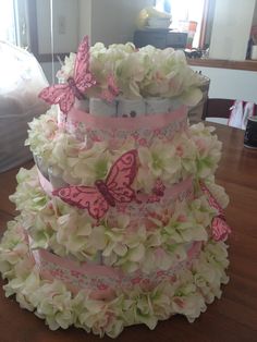 a three tiered cake with pink and white flowers on the bottom, decorated with butterflies