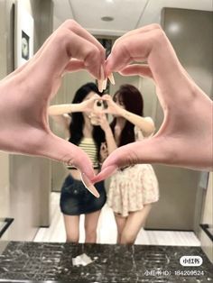 two girls are making a heart shape with their hands