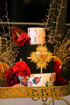 a multi - tiered cake decorated with red roses on a gold stand in front of some branches