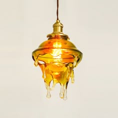 a yellow light hanging from a ceiling with drops of liquid on it and a brown cord